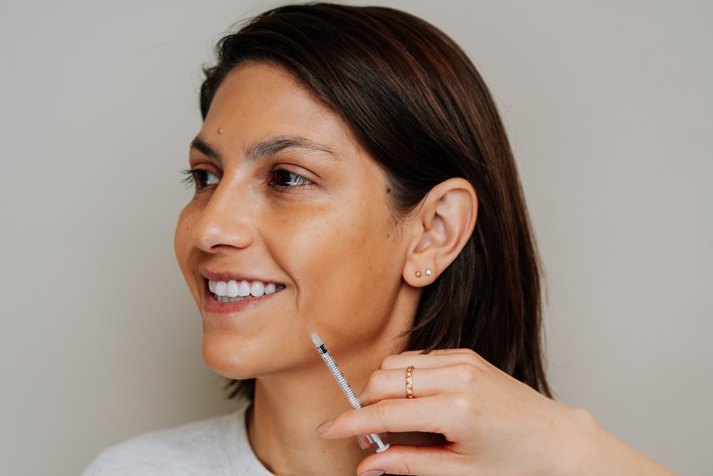 Smiling woman receiving Botox injection to side of face.