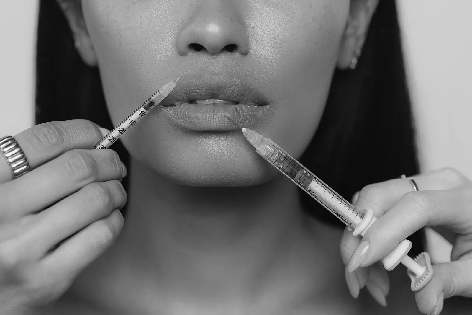 Close-up of woman’s lips in black and white holding two syringes, illustrating how long injectables last